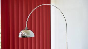 A floor lamp with a curved arm and a reflective shade against a red striped background.