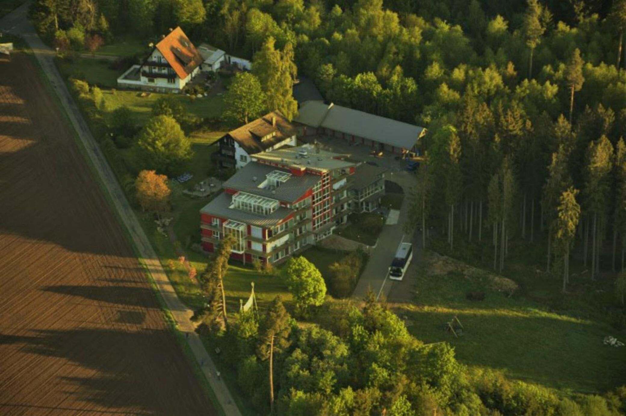 An aerial view of a large building with multiple sections, surrounded by dense forest.
