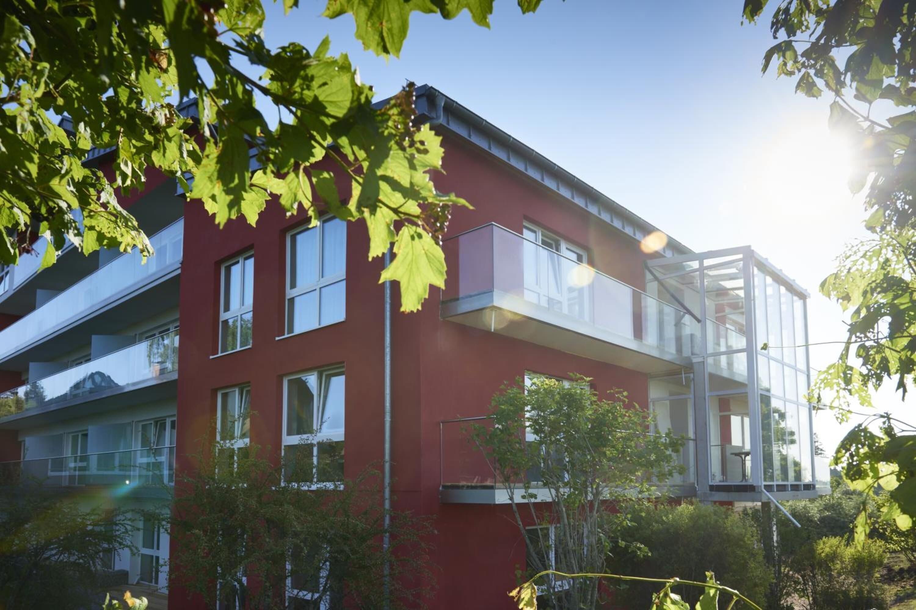 Ein modernes Gebäude mit roter Fassade, großen Fenstern und einem Glasbalkon.