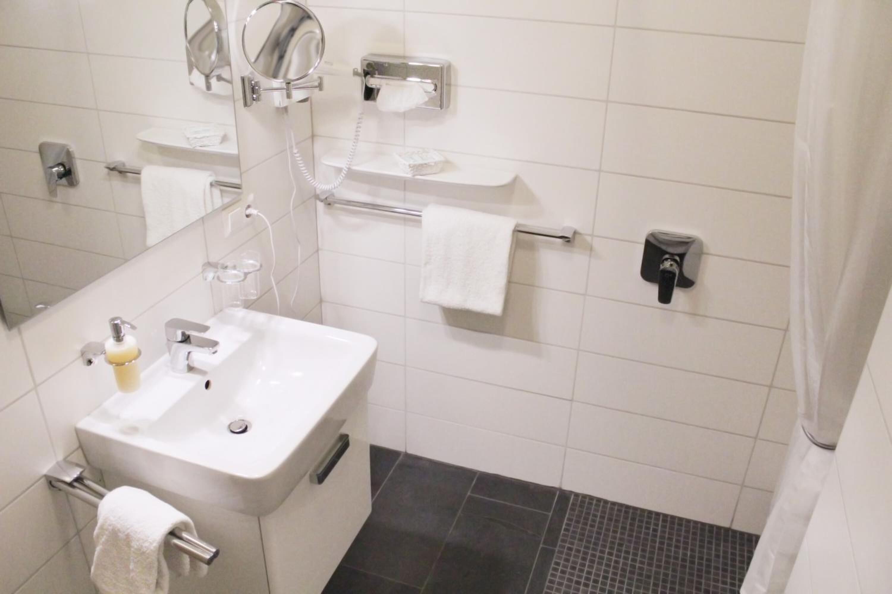Un baño con lavamanos, espejo, toallero y soporte para papel higiénico.