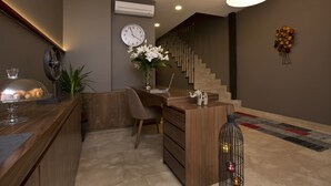A modern reception area with a wooden desk, a laptop, a clock, and a staircase in the background. - SNOG Rooms & Suites (Istanbul)