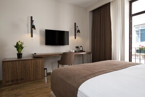 Habitación de hotel con cama, escritorio, silla, televisor y ventana con cortinas.