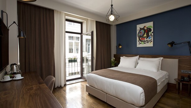 A hotel room with a large bed, a desk with a kettle, a chair, and a view through a sliding glass door. - SNOG Rooms & Suites (Istanbul)