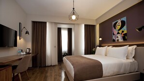 A hotel room with a wooden desk, a bed with white bedding, a flat-screen TV, and a painting on the wall. - SNOG Rooms & Suites (Istanbul)