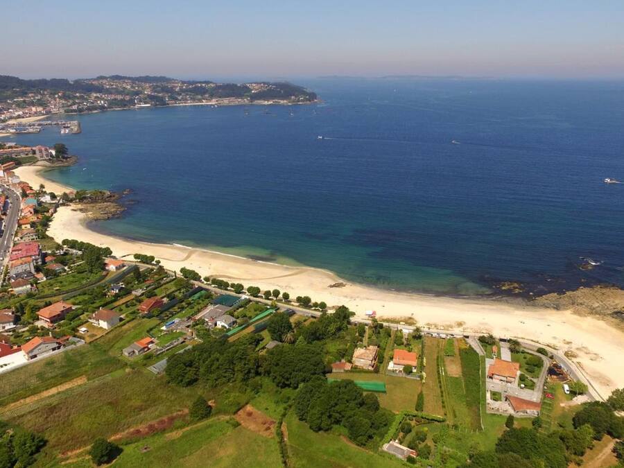 An aerial view of a coastal town with a beach, a road, and residential areas.