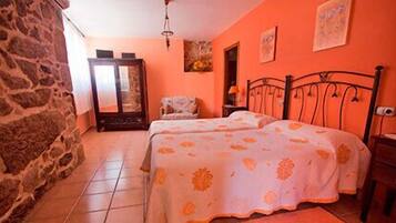 Un dormitorio con dos camas, una pared de piedra, una puerta de madera y una pequeña silla.