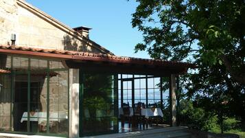 A stone building with a glass enclosure, outdoor seating, and a view of the sea.