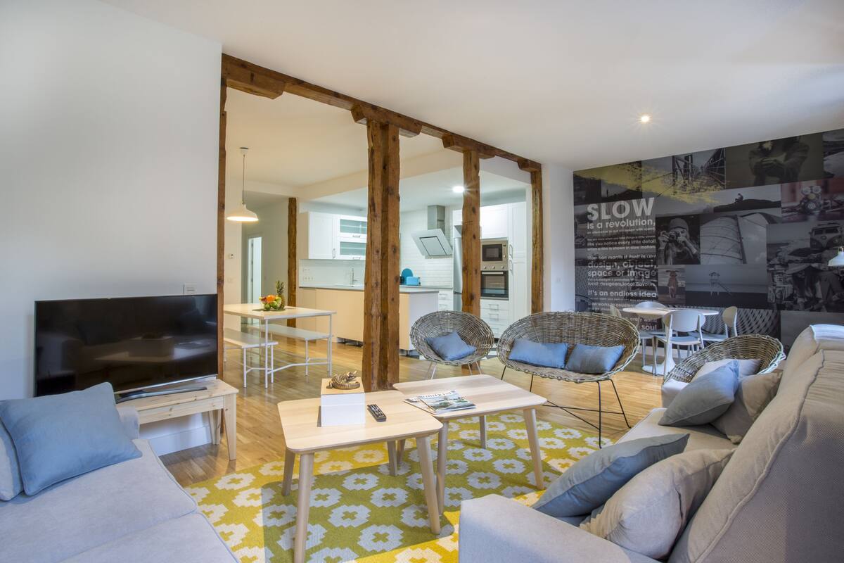 A modern living room with a flat-screen TV, sofa, and wicker chairs.