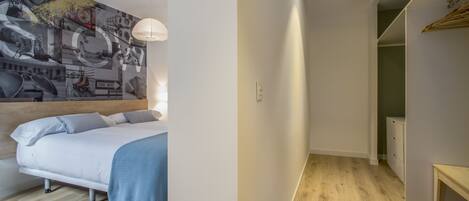 Un dormitorio moderno con una cama, una pared con un mural de un paisaje urbano y un pasillo que lleva a un armario.