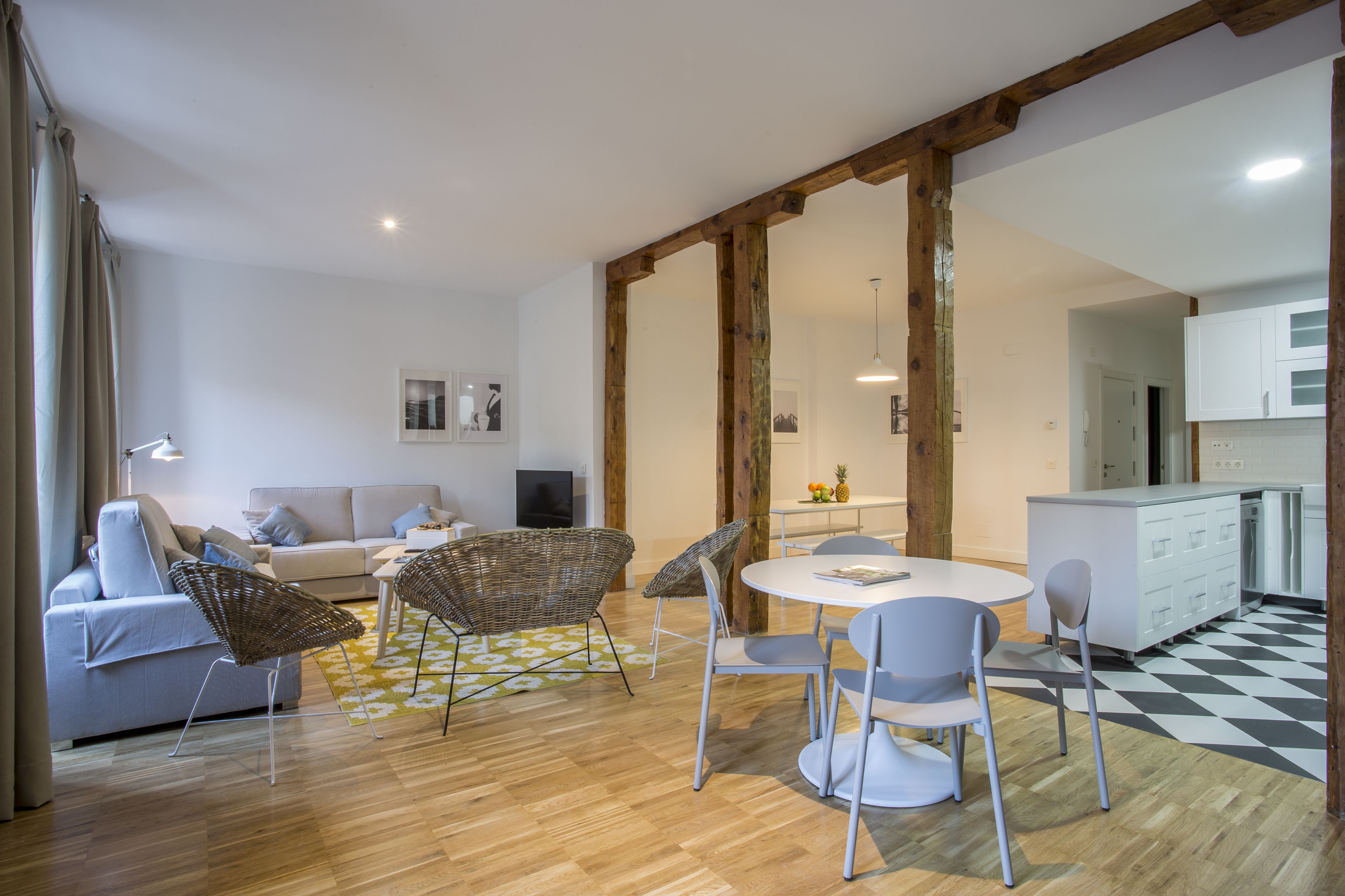 A modern living room with a sofa, wicker chairs, a dining table, and a kitchen area with white cabinets.