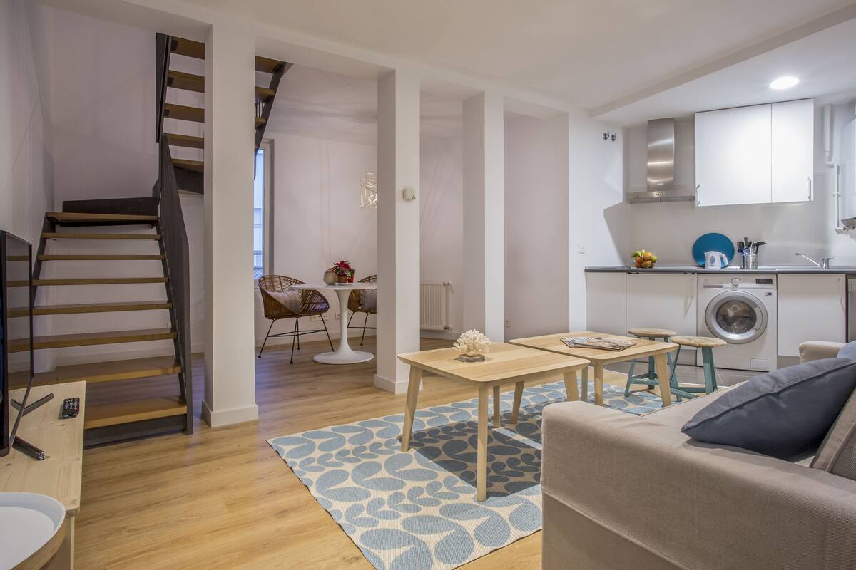 A modern apartment with a staircase, a dining area, a kitchen, and a living room.