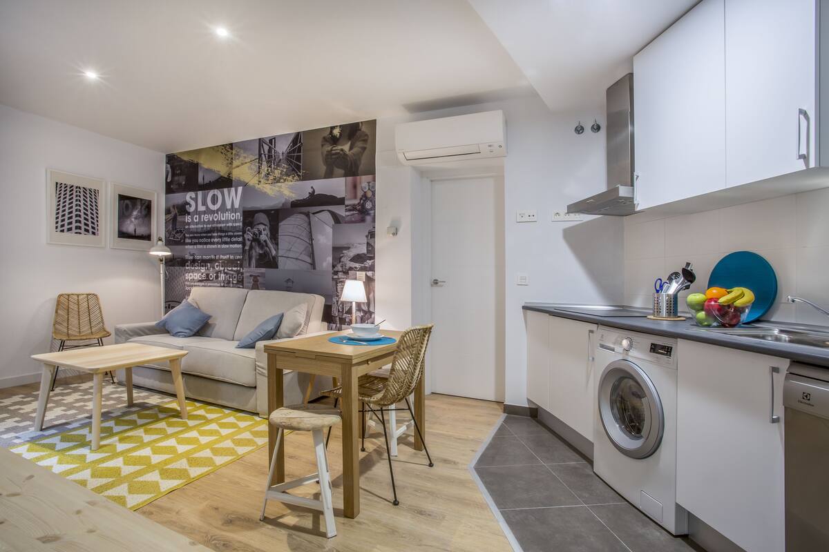 A compact living space with a sofa, a dining table, a washing machine, and a kitchen area.