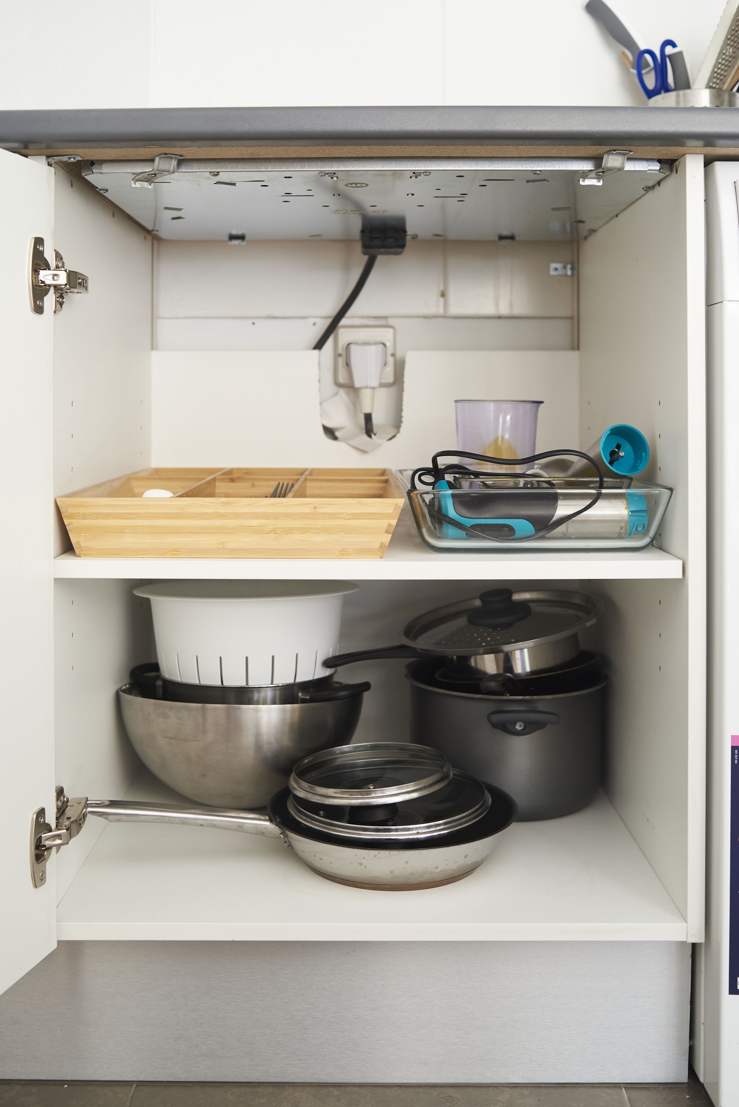 Una cocina con armarios blancos, tabla de cortar de madera, licuadora y varias ollas y sartenes.