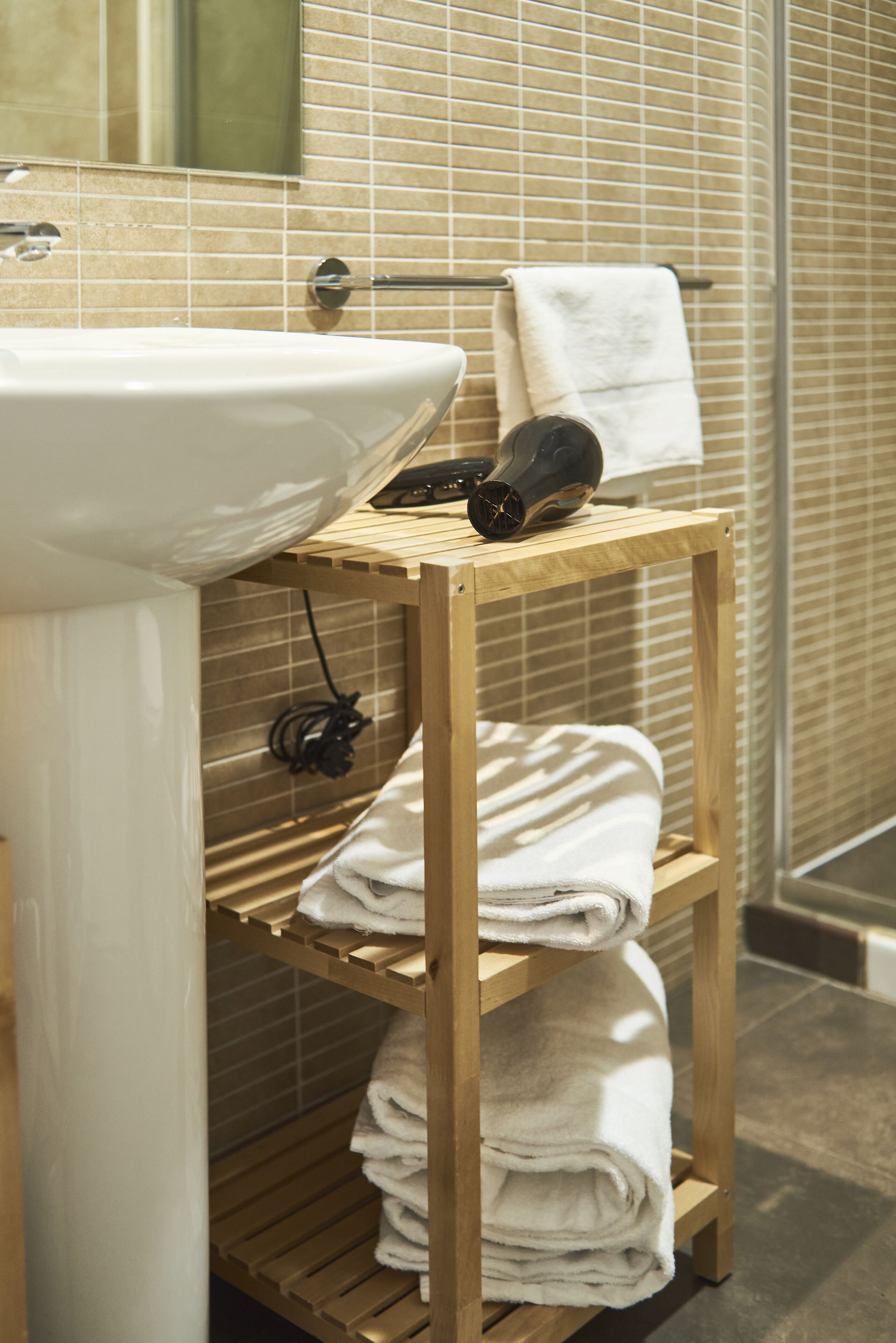 A bathroom with a sink, a wooden shelf with towels, and a towel hanging on a rack.