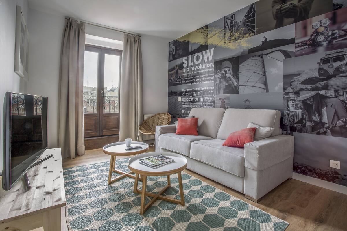 A living room with a sofa, two side tables, a television, and a large wall mural.
