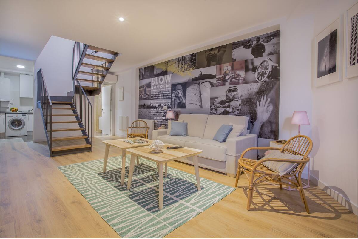 A modern living room with a staircase, a sofa, a coffee table, and a large wall mural.