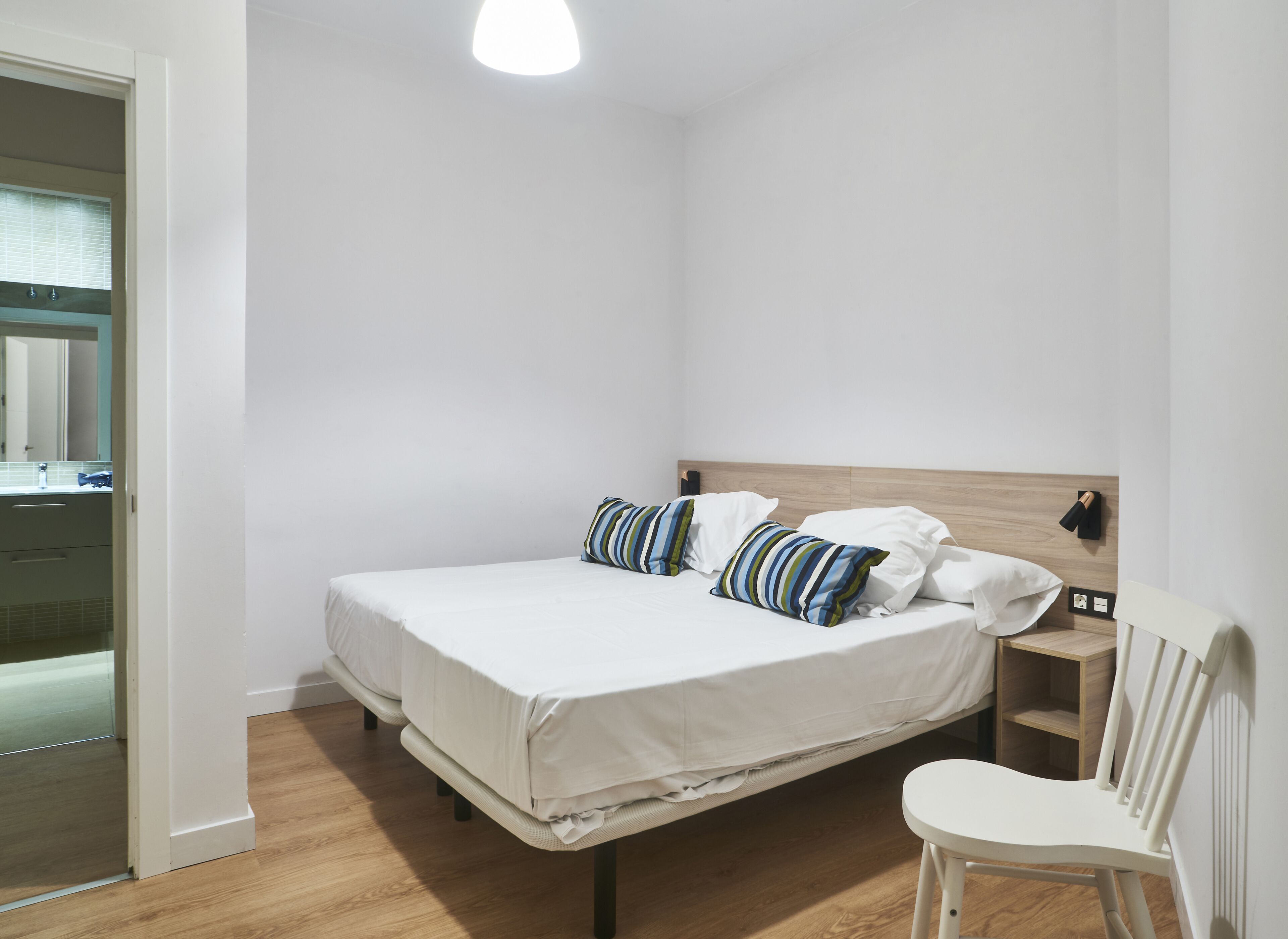 A bedroom with a bed, a nightstand, a chair, and a wooden headboard.