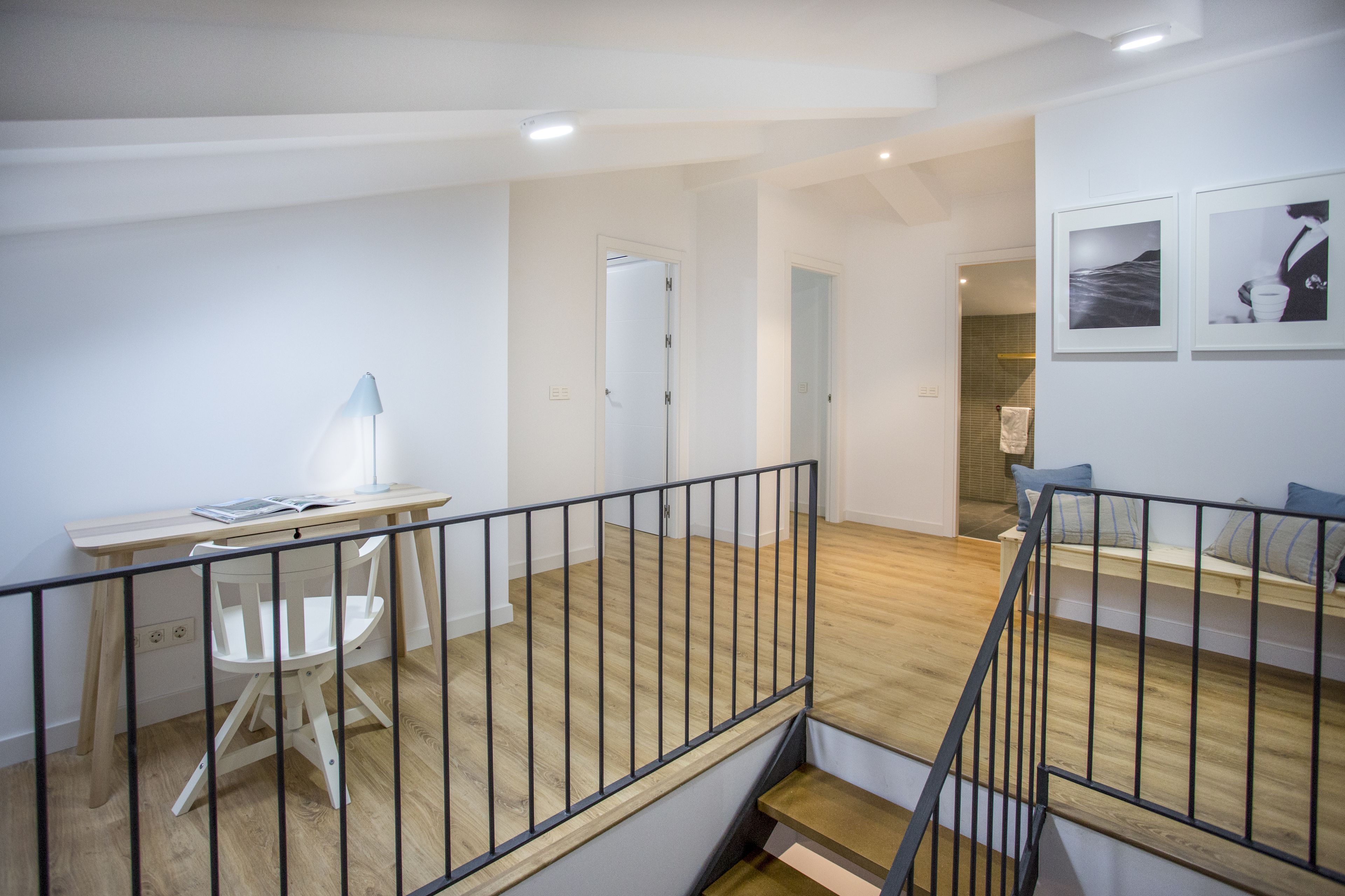 Une pièce spacieuse avec un bureau en bois, une chaise blanche et une rambarde noire.