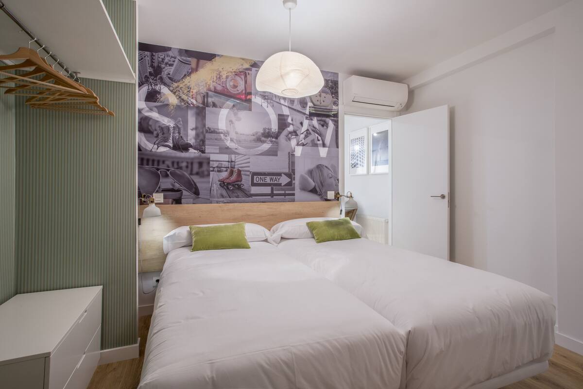 A bedroom with a large bed, a wooden headboard, a wall mural, a hanging light fixture, and a wardrobe.