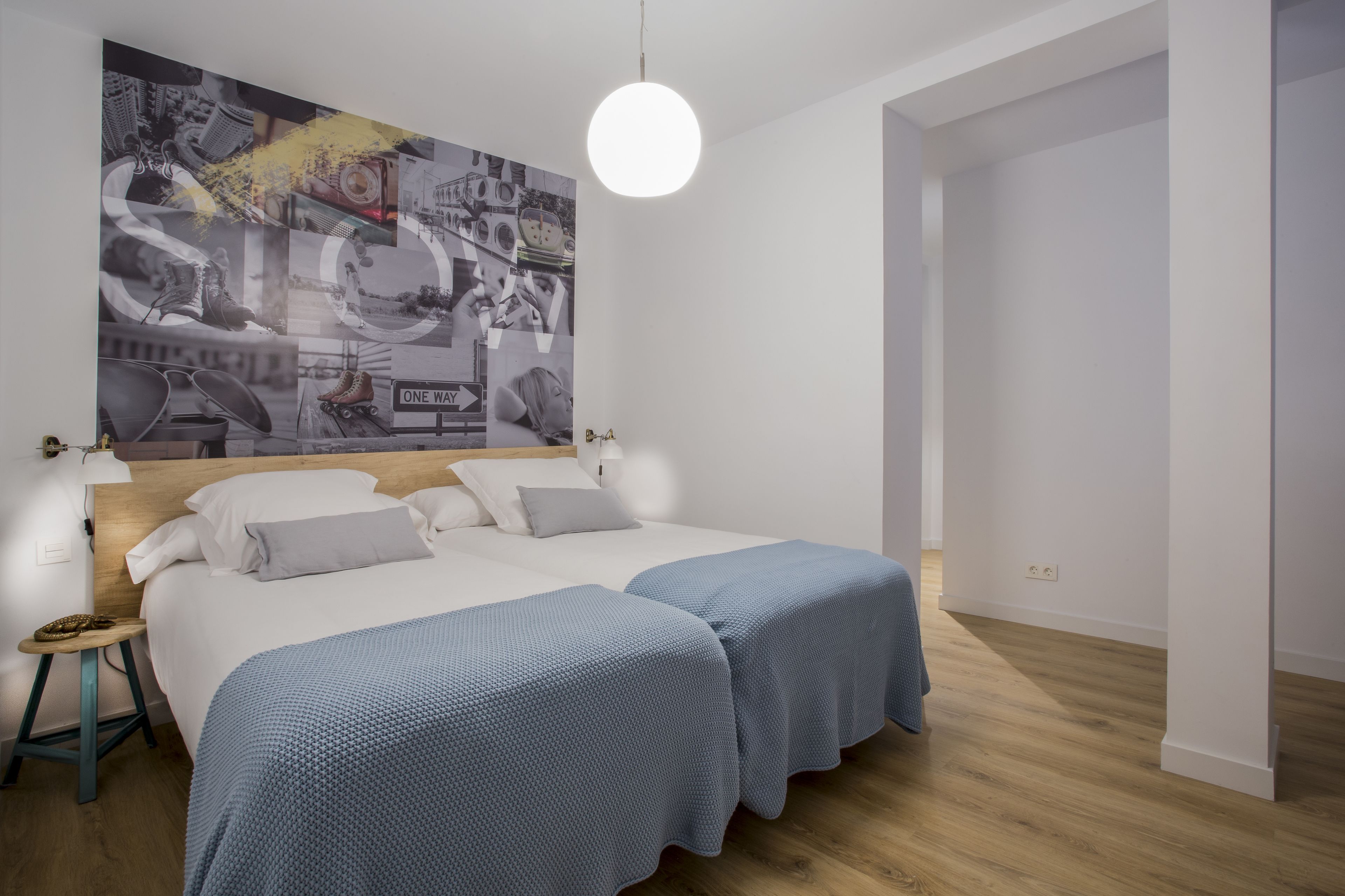 Un dormitorio moderno con dos camas, una gran obra de arte abstracta en la pared y una lámpara de techo redonda.