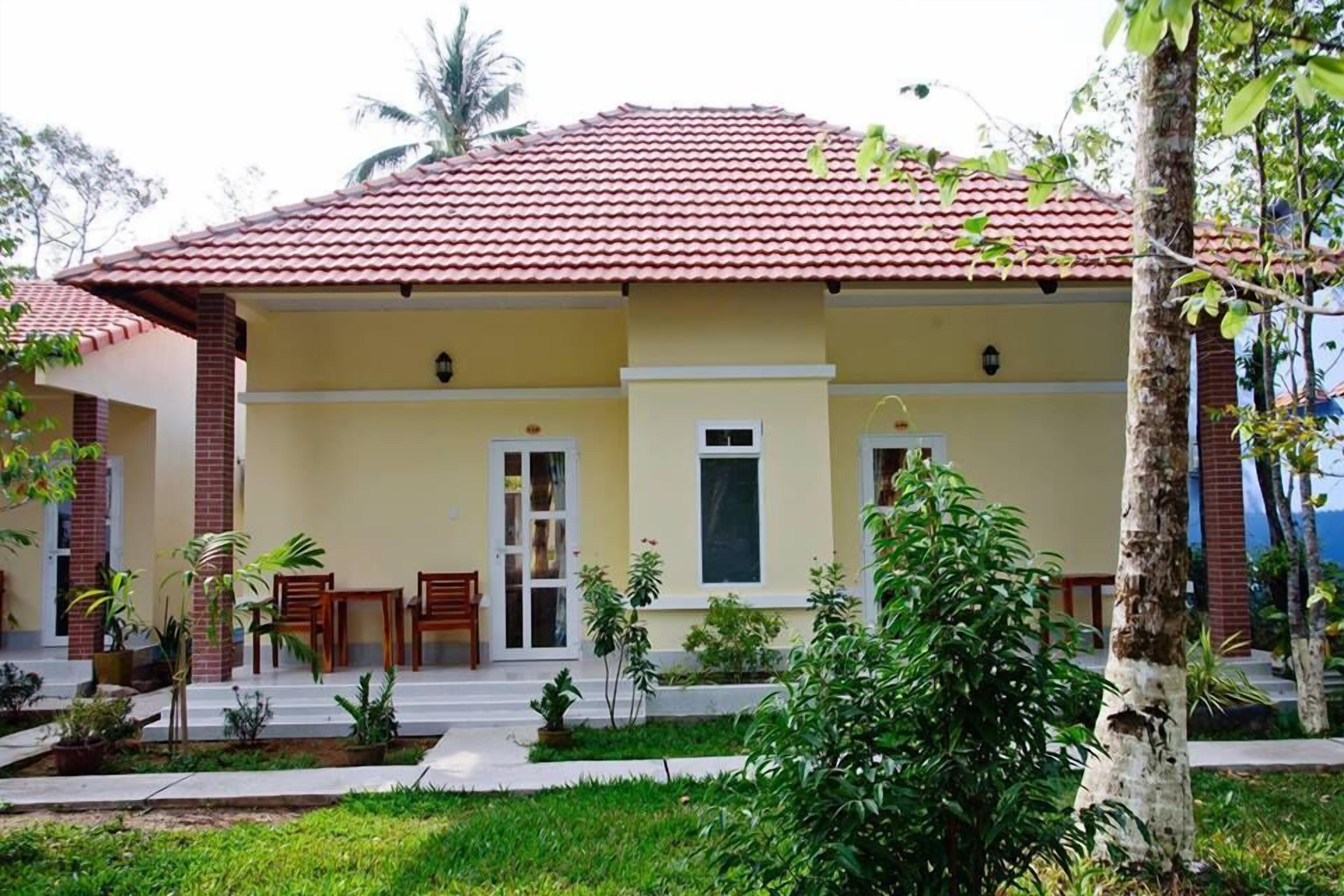 A two-story building with a red-tiled roof, a yellow facade, and a covered porch with chairs.