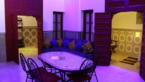 An open-plan living area with a round table and chairs, a sofa with cushions, and patterned walls. - Riad Meftaha (Rabat)