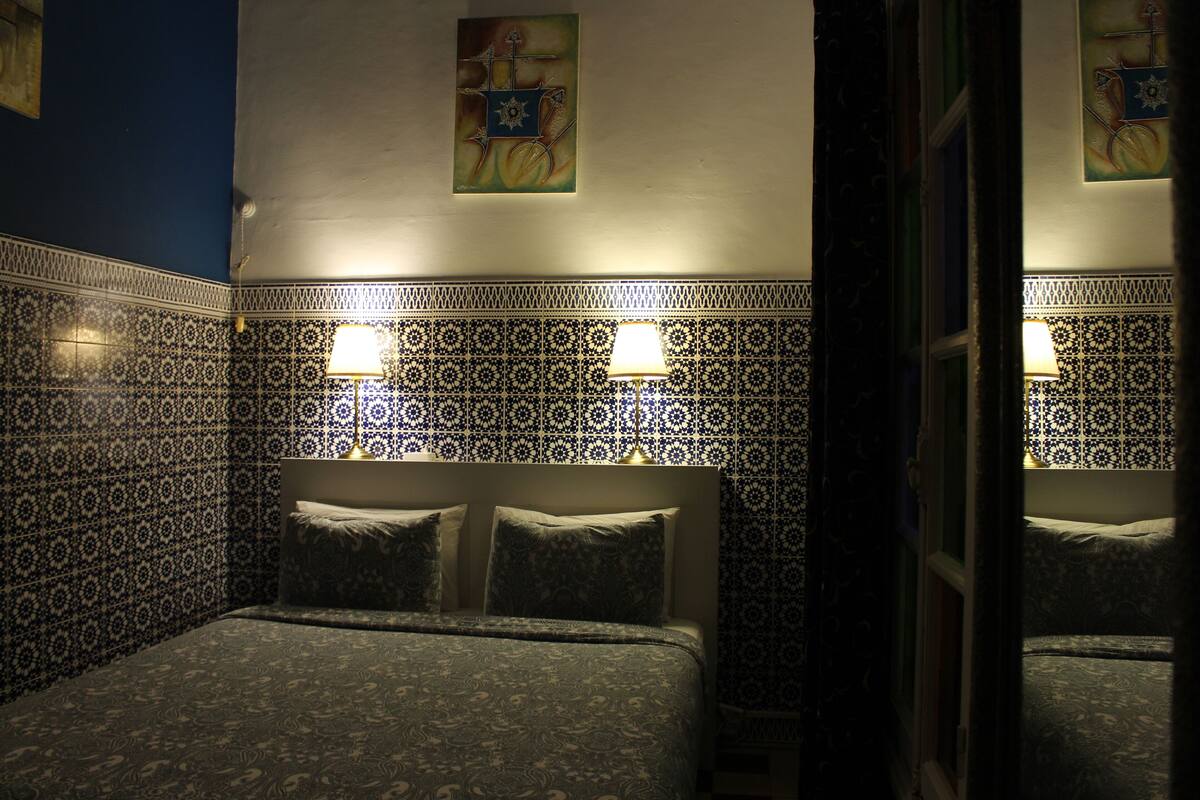 A hotel room with a patterned tile wall, a bed with a headboard, and two wall-mounted lamps.