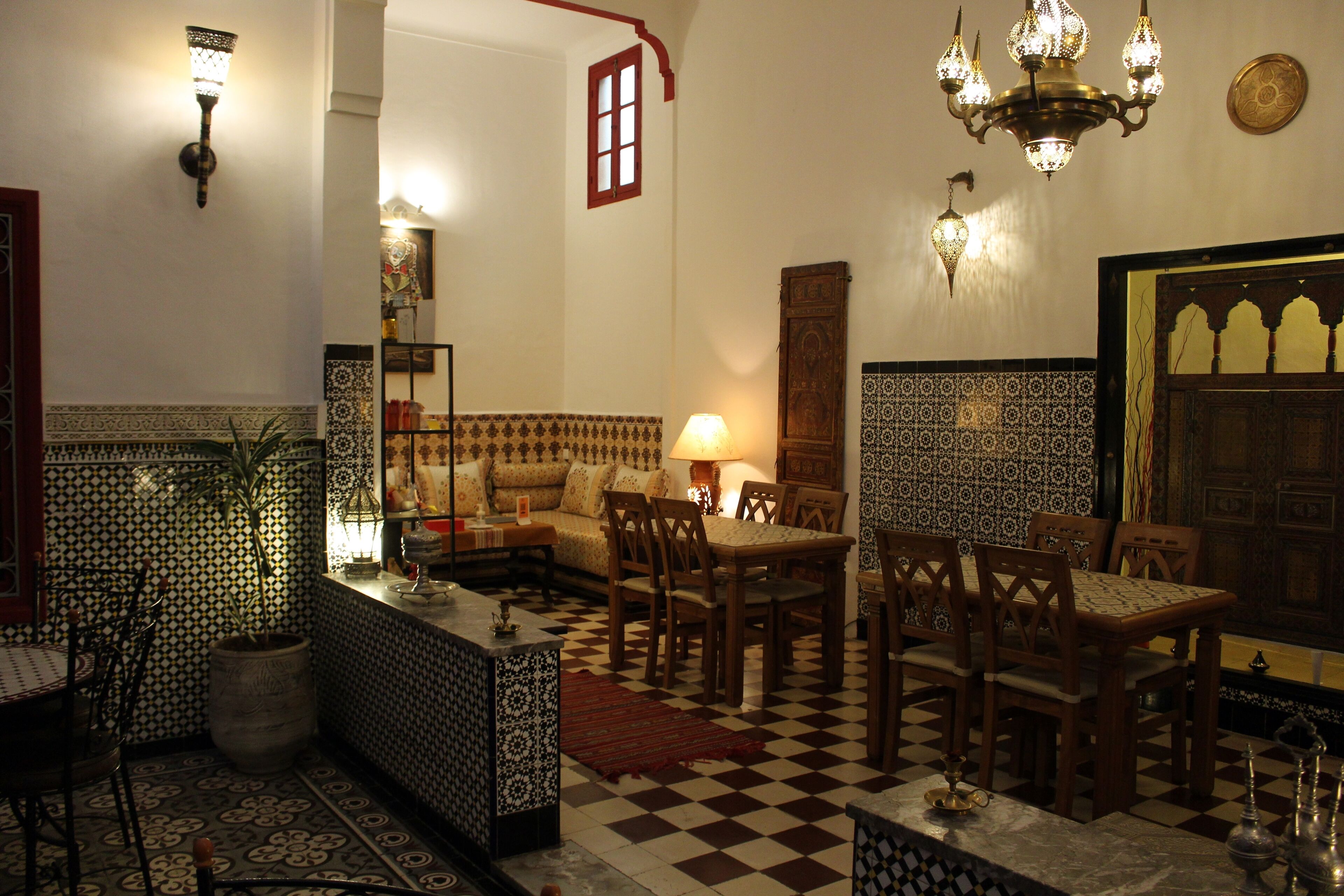 A traditional Moroccan interior with patterned tiles, a checkered floor, wooden furniture, and decorative lighting.