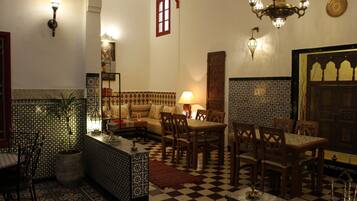 A traditional Moroccan interior with patterned tiles, a checkered floor, wooden furniture, and decorative lighting.