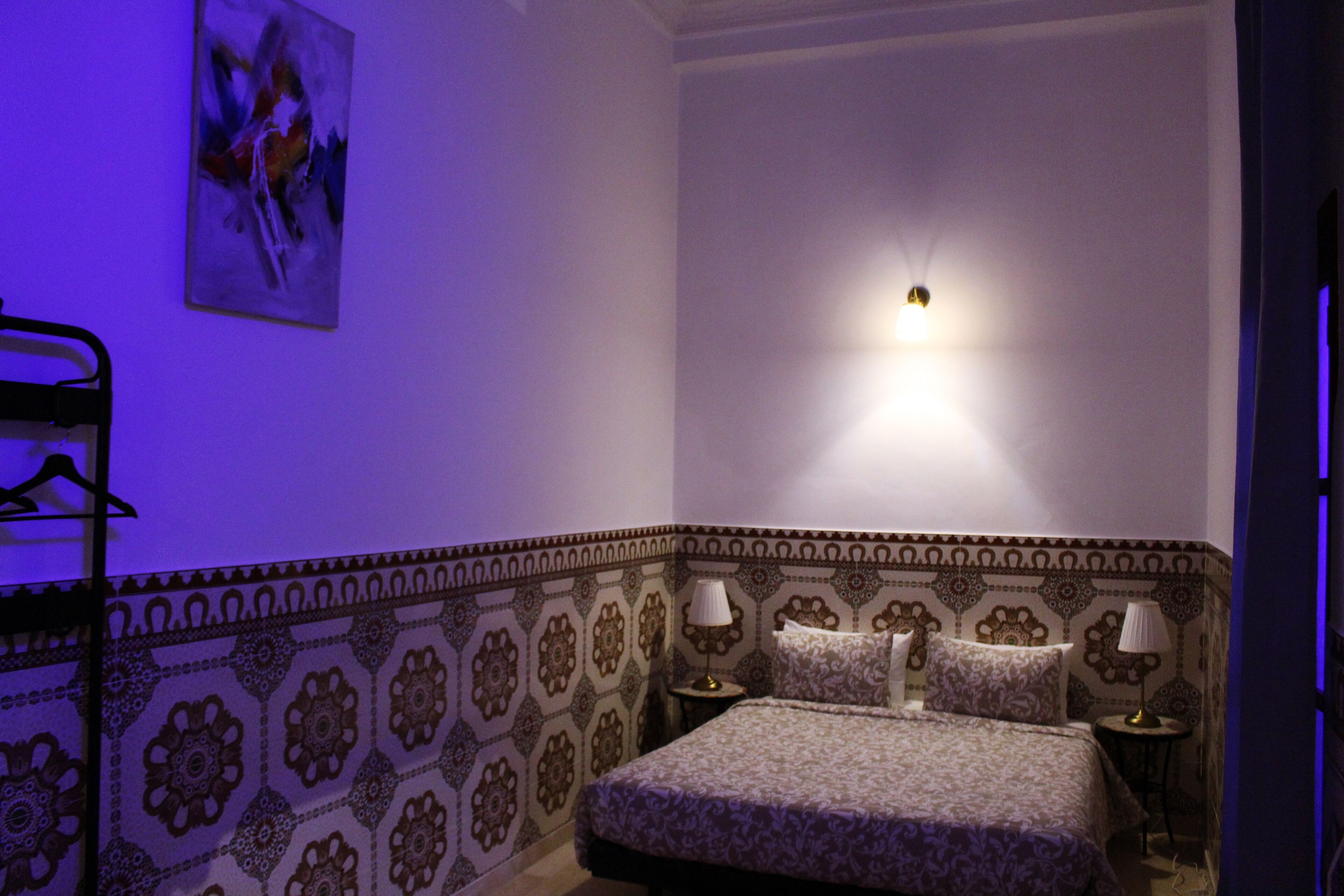 A bedroom with a patterned wall, a bed with two pillows, two bedside tables with lamps, and a wall-mounted light fixture.