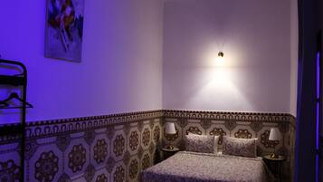A bedroom with a patterned wall, a bed with two pillows, two bedside tables with lamps, and a wall-mounted light fixture.