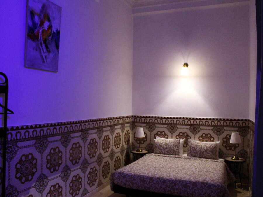 A bedroom with a patterned wall, a bed with two pillows, two bedside tables with lamps, and a wall-mounted light fixture.