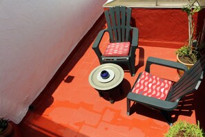 A small outdoor seating area with two chairs and a table, surrounded by a red wall and potted plants.