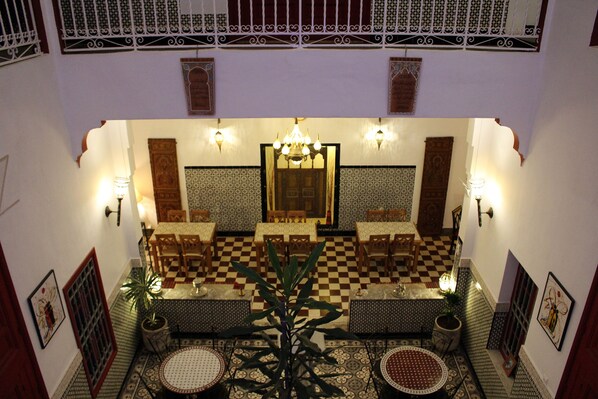 A traditional Moroccan interior with checkered flooring, ornate wooden furniture, and a central chandelier.