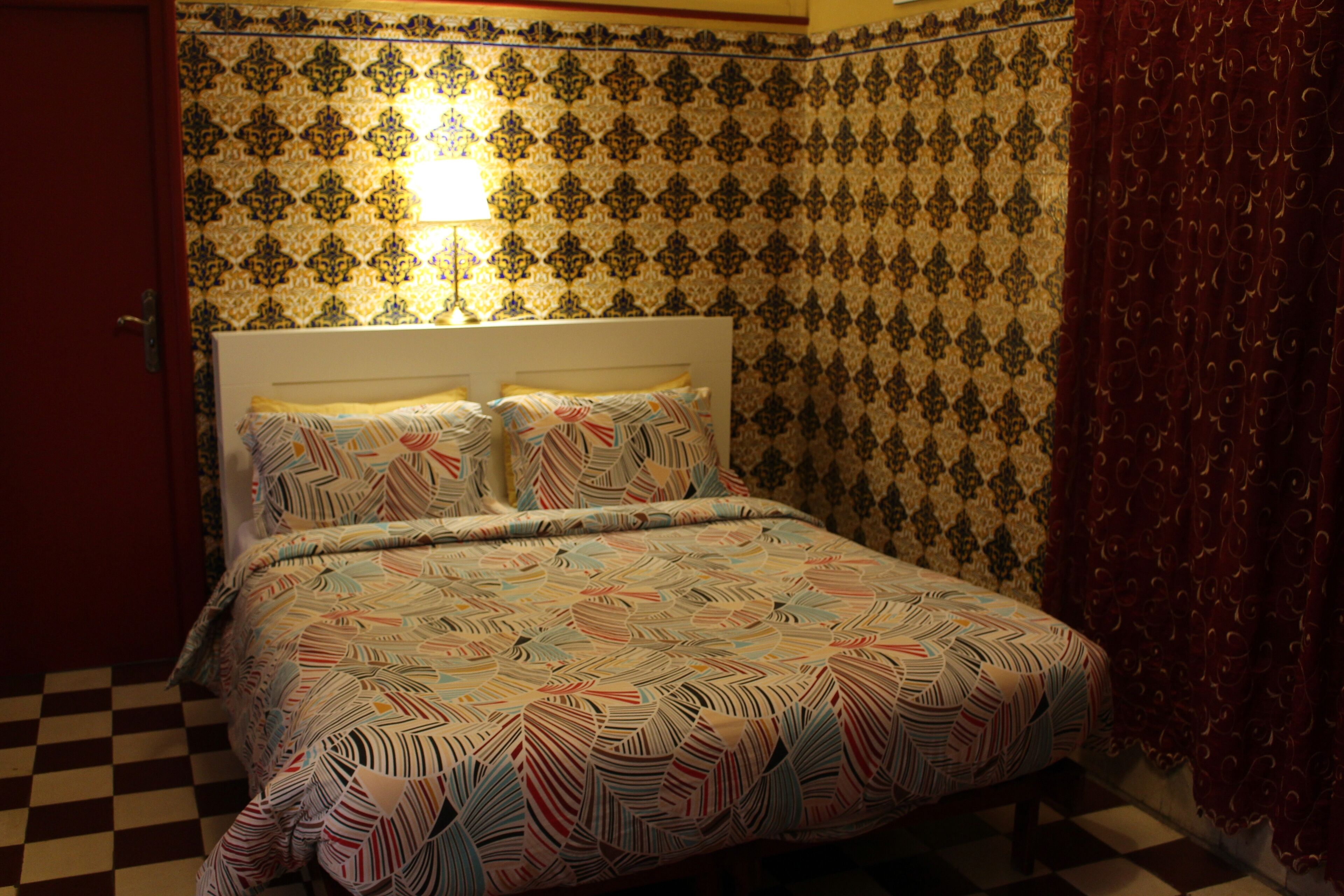 A bed with a patterned bedspread, a headboard, and a wall with a patterned wallpaper.