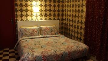 A bed with a patterned bedspread, a headboard, and a wall with a patterned wallpaper.