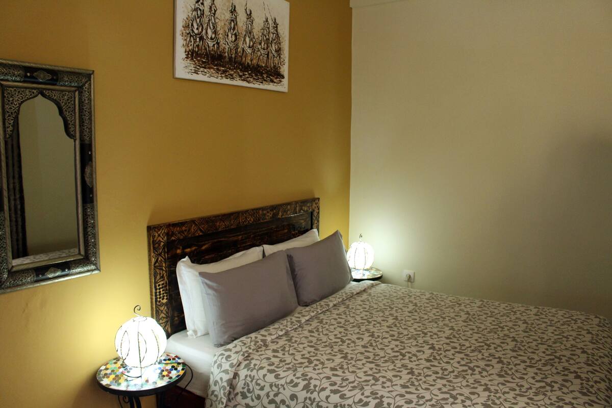 A bedroom with a bed, two bedside lamps, a mirror, and a framed artwork on the wall.