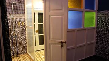 Een badkamer met betegelde vloer, een douchegedeelte en een deur met hendel.