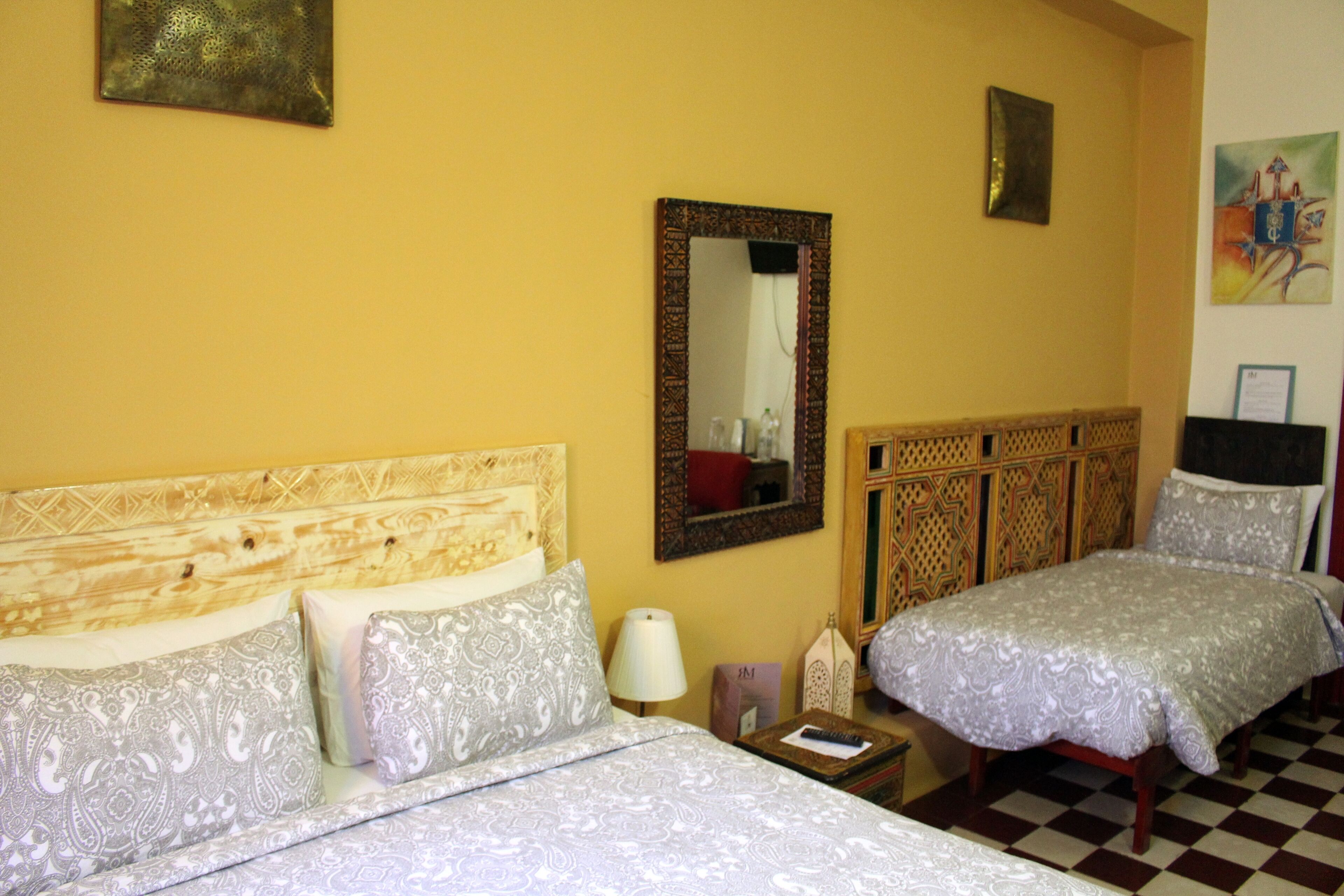 Ein Hotelzimmer mit einem hölzernen Kopfteil, zwei Betten mit gemusterten Bettbezügen, einem Spiegel und einem karierten Boden.