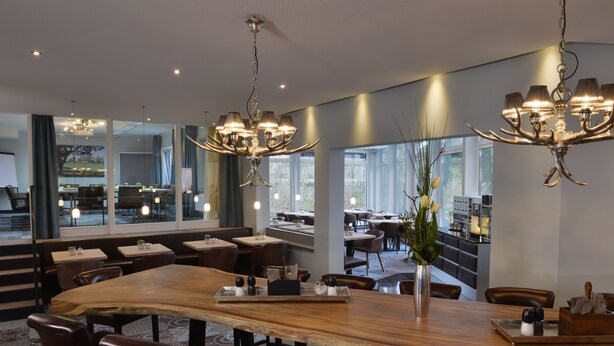 En moderne restaurant med et stort træbord, læderstole og en lysekrone.