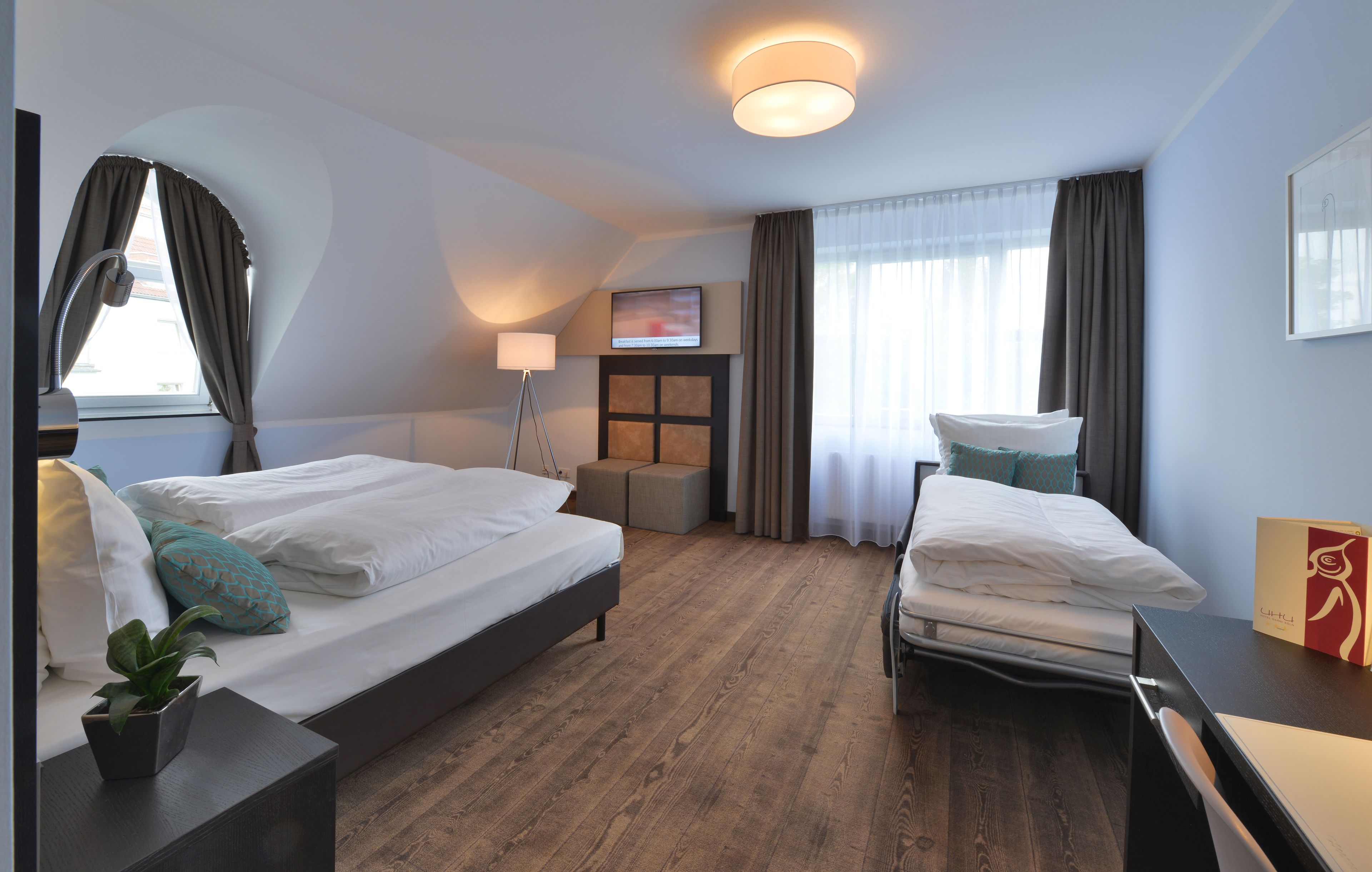 A hotel room with two beds, a desk, a lamp, a TV, and a window with curtains.
