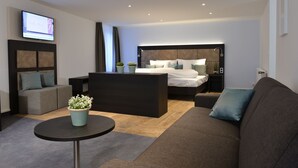Et moderne hotelværelse med seng, sofa, sofabord og et fjernsyn ophængt på væggen.
