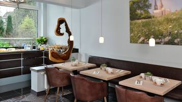 Un comedor moderno con mesas de madera y sillas de cuero marrón, un adorno de madera en la pared y un ventanal con vistas a zonas verdes.
