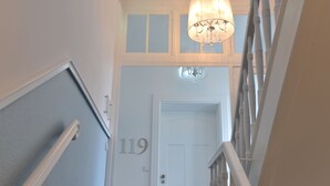 En trappe med en hvid dør mærket med nummer 119, en lysekrone og et gelænder.