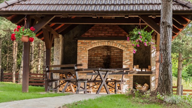 A rustic outdoor pavilion with a brick fireplace, wooden benches, and hanging flower baskets. - House Rustico (Plitvicka Jezera)