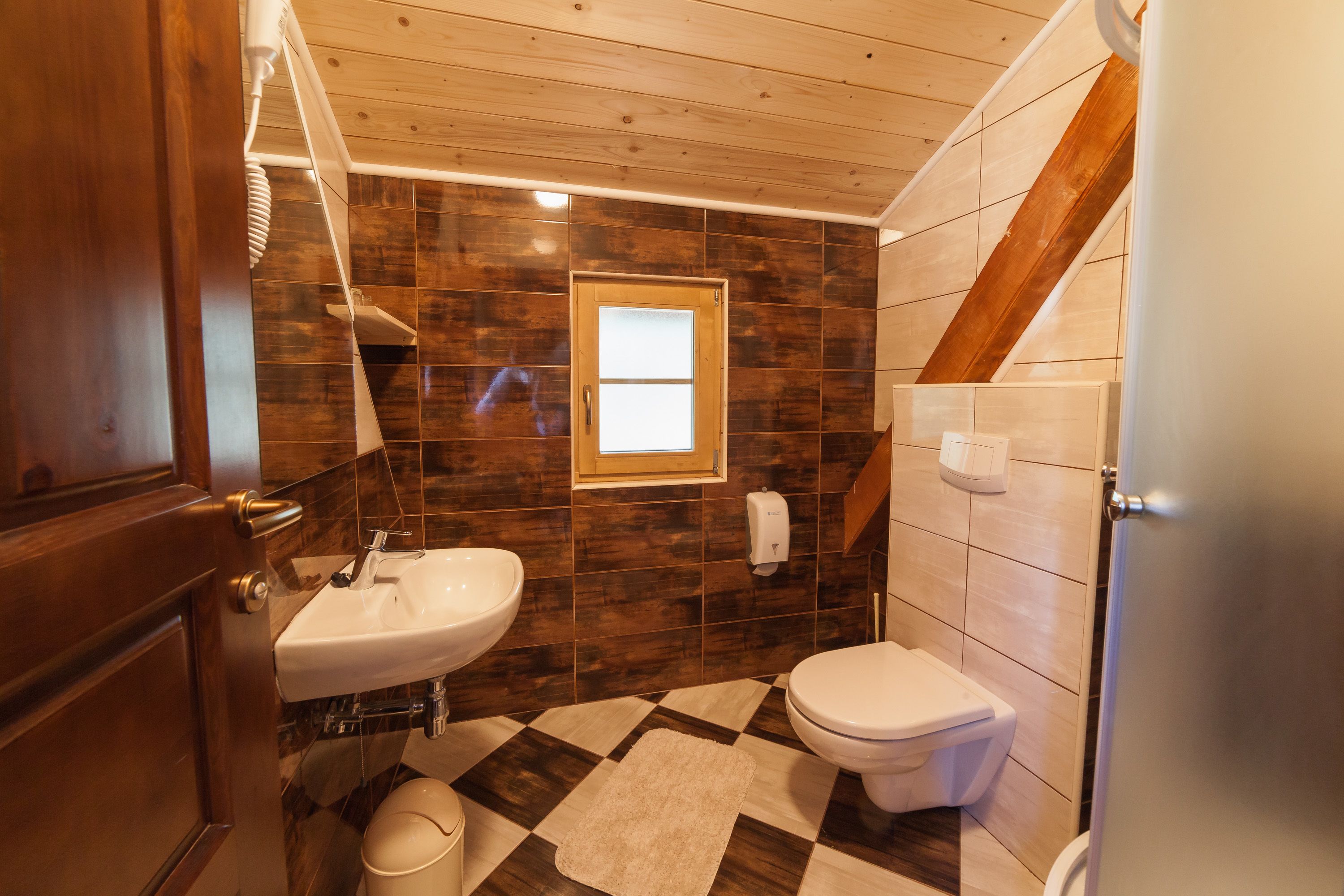A bathroom with a wooden ceiling, a checkered floor, a sink, and a toilet.