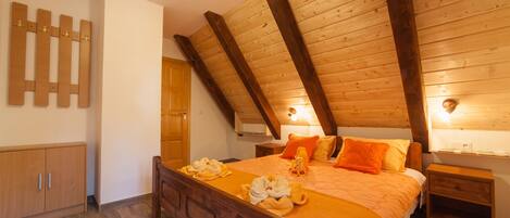 A bedroom with a wooden ceiling, a bed with orange bedding, a nightstand, and a wooden wardrobe.