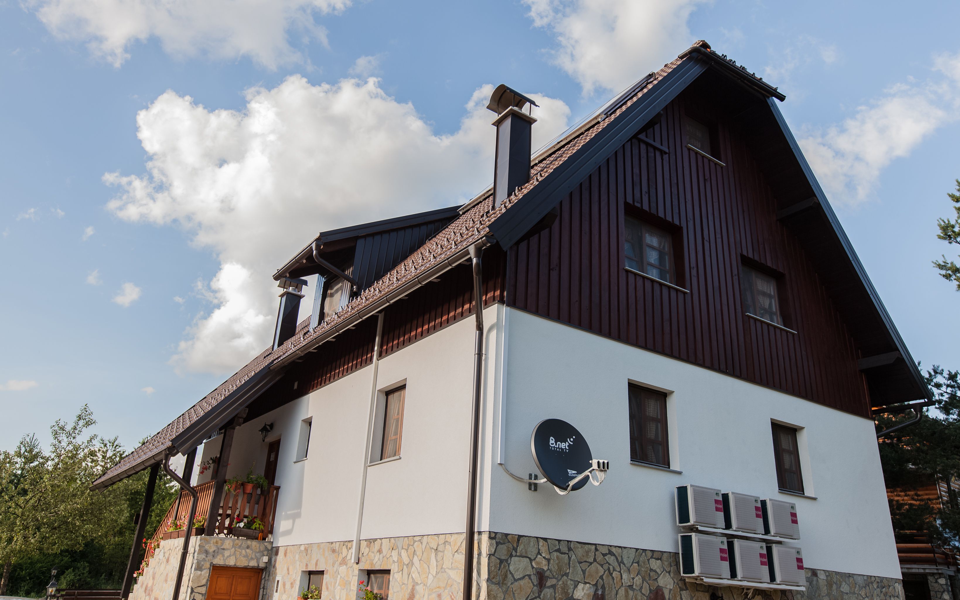 Ein zweistöckiges Gebäude mit einer Steinfassade, einem Holzbalkon mit Topfpflanzen und einer montierten Satellitenschüssel.