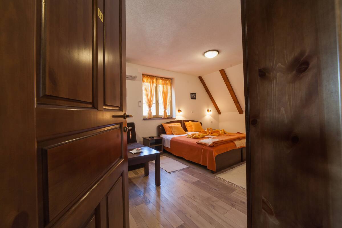 Quarto com cama, mesa de cabeceira e janela com cortinas.