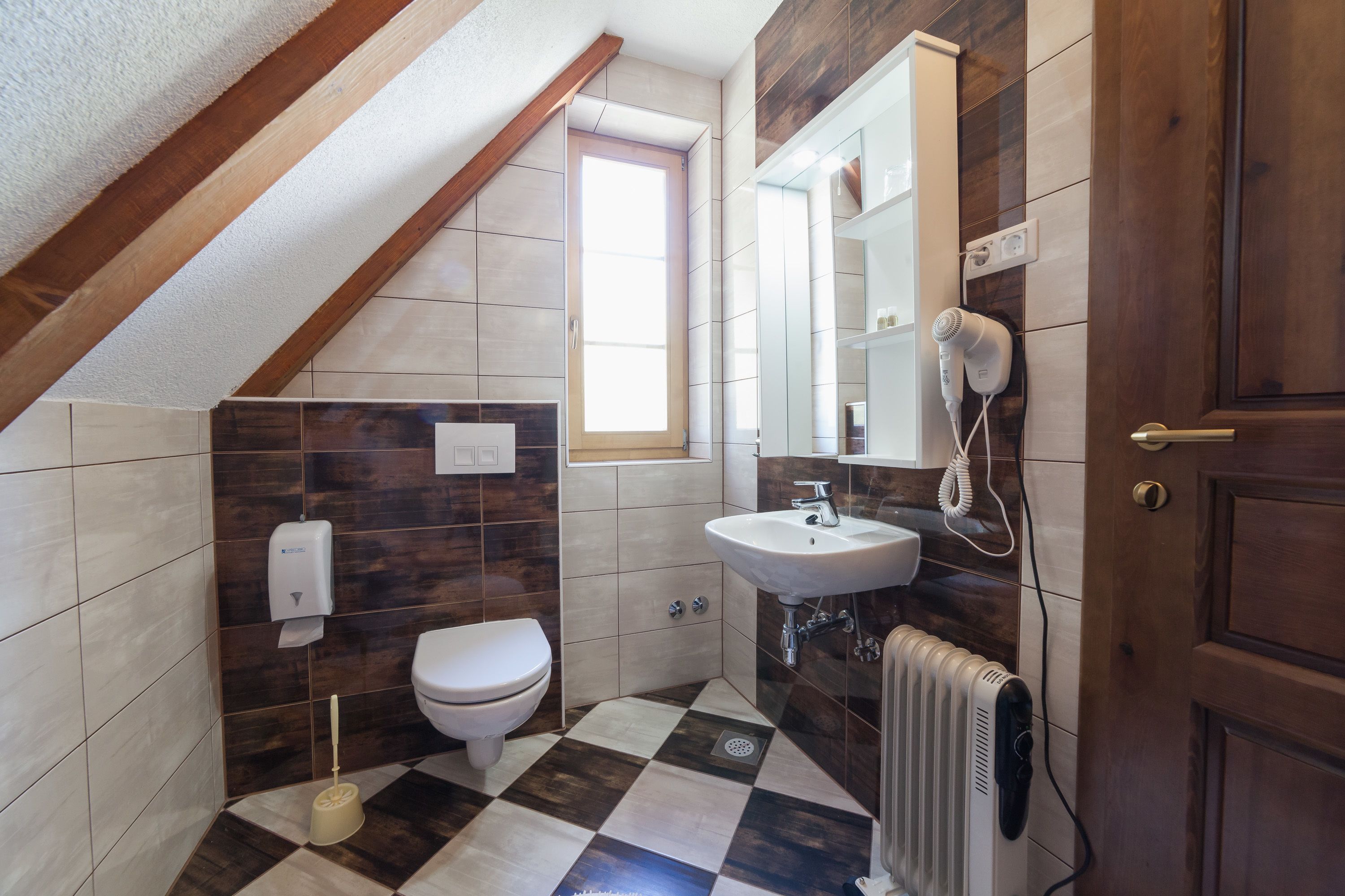 Un baño pequeño y moderno con suelo de cuadros, inodoro blanco, lavabo y radiador.